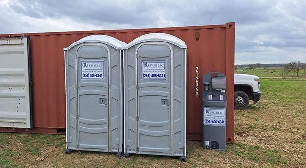 Array of blue and gray portable toilets arranged in a storage yard