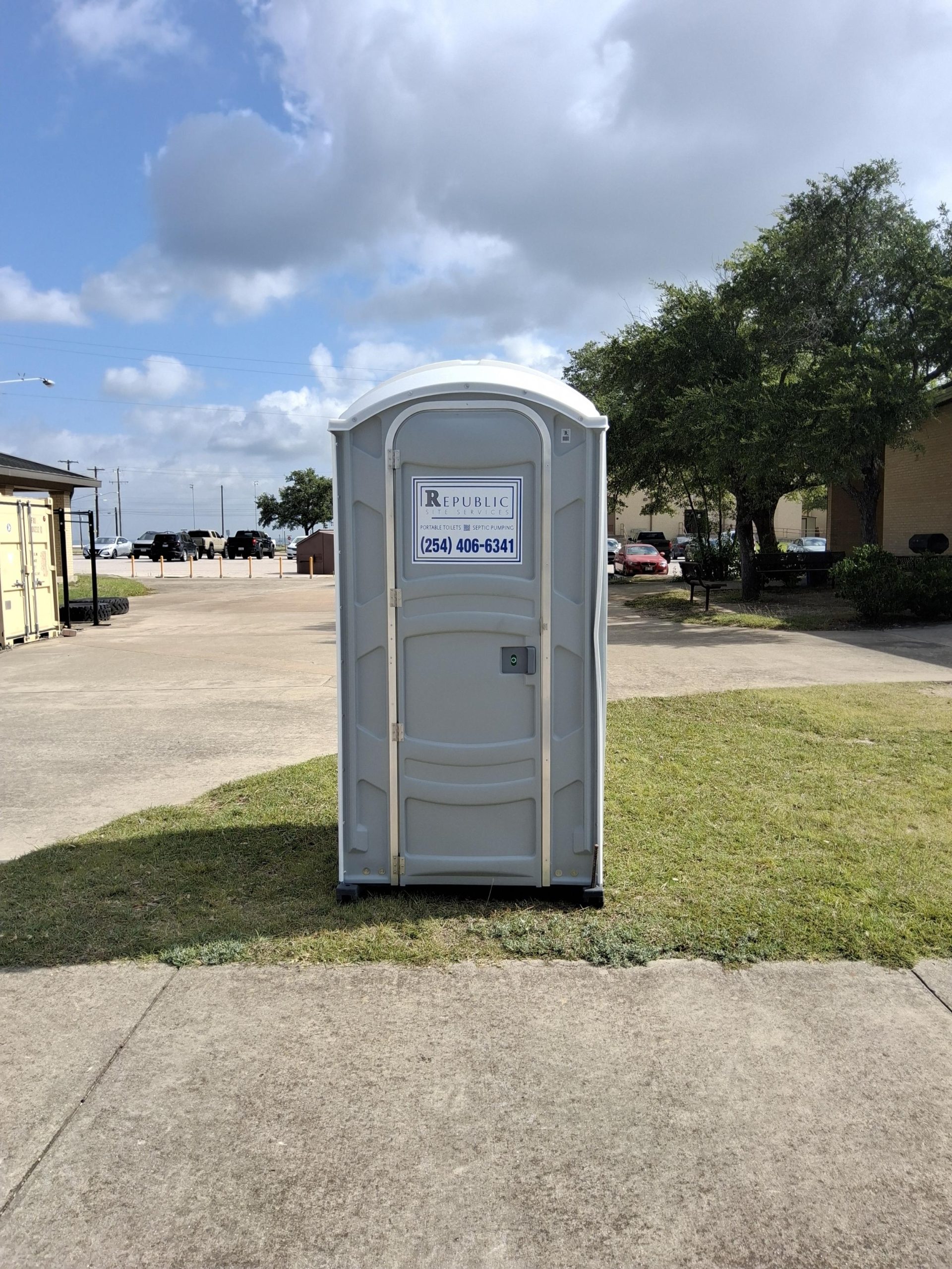 Single Portable Toilet on a Concrete Path Under a Cloudy Sky