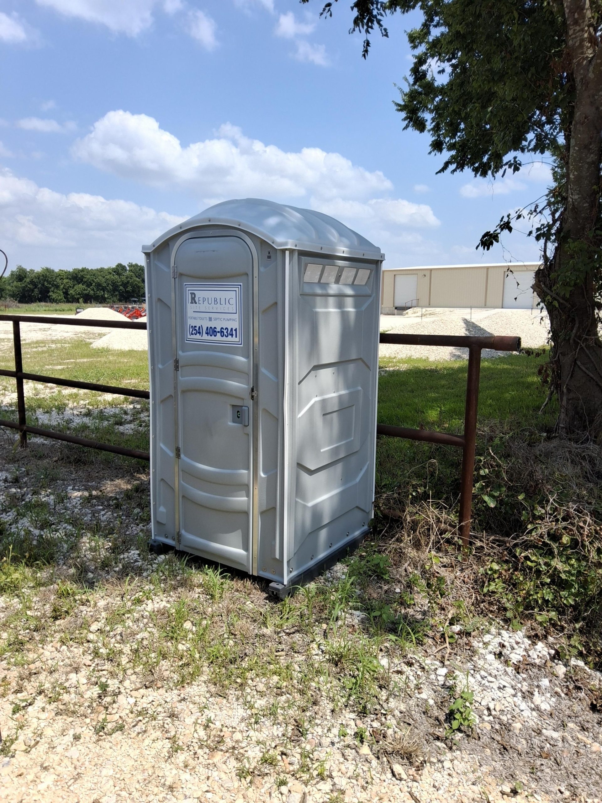 Portable Toilet Rental Unit Placed Outdoors Alongside a Fenced Area