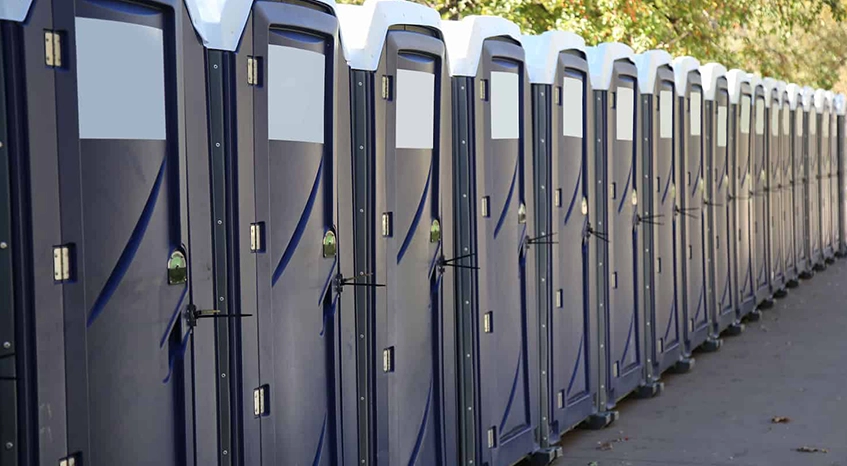 Row of Blue Portable Restrooms Outdoors Under Trees