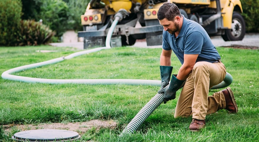 Worker Performing Septic Pumping Services with Truck in Background