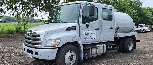 Septic Service Truck Parked on Gravel Road Near Green Trees