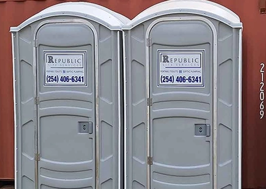 Two Gray Portable Toilet Rentals with Business Signage and Contact Information