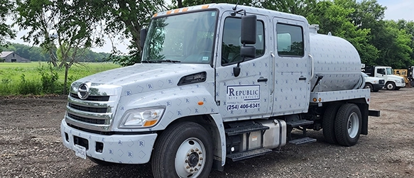 Septic Pumping Truck Parked on Gravel Lot Near Green Trees