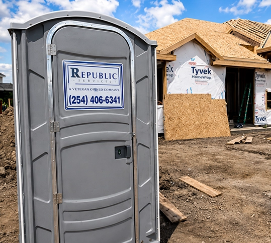 Portable Toilet on Construction Site with Wooden Framed Building in Background